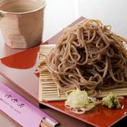飯山市【富倉そば】の主人、そば打ち名人・阿部竹一氏の手打ちそばです。蕎麦の実を石臼で引いた蕎麦粉、つなぎには小麦粉は使用せず、雄山火口（山ごぼう）の葉脈を0.3～0.5％だけ混ぜています。