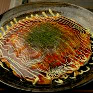 豚、海老、烏賊が入ったお好み焼きです。口に入れるとふわとろの柔らかさ。次にまろやかな卵の味わいとキャベツの甘みが広がります。生地を鉄板に広げてから具を乗せ、何層も生地を重ねて焼き上げるお好み焼きです。