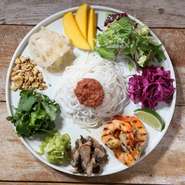 特製の海老味噌ソースをのせたベトナムの米細麺ブンを中心に、マリネしグリルしたトムヤムシュリンプ、色とりどりの野菜やハーブをパレットのように盛り付けた、ヘルシーに食べられるサラダヌードルプレート。