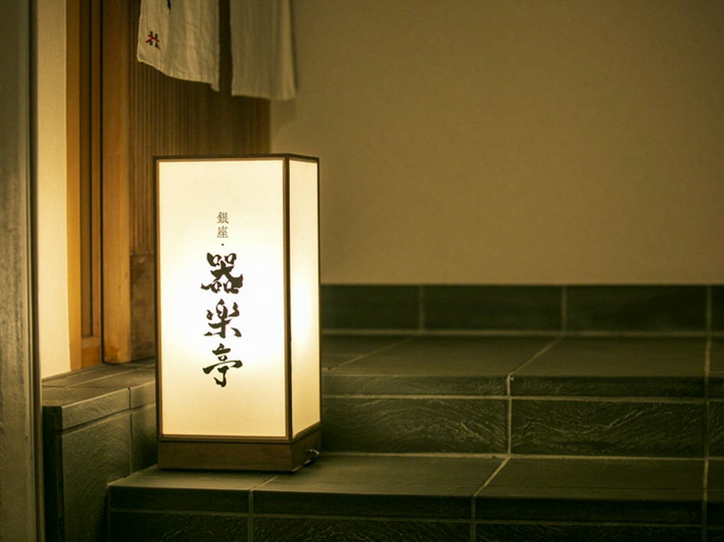 ビルの上階でひっそり灯る行灯と、風情ある引き戸が印象的