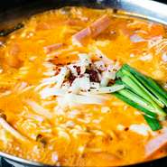 韓国の軍隊鍋『プデチゲ』。軍隊生活で食べる鍋を再現。辛い鍋にソーセージや野菜をどっさり入れ、乾麺を煮込んでいます。甘みのあるピリ辛味が後を引き、いつの間にかやみつきに。