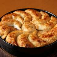 餃子を敷き詰めた鉄鍋に、なみなみと油を注いで揚げ焼きにしていきます。高い位置からたっぷりの水で加えることで、炎が餃子を包み込みサッと蒸して完成。表面はカリッモチッ！