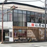 山口市の湯田温泉街の大通り、湯田温泉一丁目交差点のカドにある焼肉店が【万両厚味】です。複合ビルの2階にあり、カウンター6席とテーブル20席の全26席が用意されています。