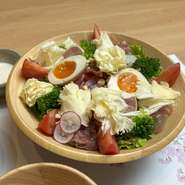 たっぷりの野菜の中で花びらのようにカットされたチーズと温玉、そしてトマトが彩りよく配置され食欲をそそるサラダです。特製シーザードレッシングをかけて野菜の触感とチーズと生ハムのコクが感じられるサラダです