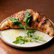 モッツアレラチーズ、リコッタチーズ、トマトソース、サルシッチャ、舞茸、ブロッコリー、パルミジャーノ、セルバチコの包み焼ピッツア。通常のピッツアより低温でじっくり焼き上げる特別なピッツアです。