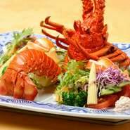 ボイルされた伊勢海老と新鮮な野菜に特製ドレッシングを添えて。新鮮でみずみずしい野菜が周囲を彩り、その中央では色鮮やかな朱色の伊勢海老が存在感を示しています。