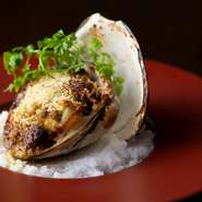 写真は、その日仕入れることができた「青森県産　活ホッキ貝」。薫り高いエスカルゴバターとパン粉を載せてじっくり焼き上げ、貝の弾力と旨みを楽しめます。
※料理は一例。食材によって内容は変わります。