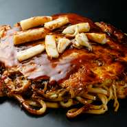 クレープ状の薄焼き生地に、たっぷりキャベツと肉、卵、麺などの具材を重ねてぎゅうぎゅう焼いた『広島お好み焼き』は、大阪では少し珍しい存在。繊細な温度管理が叶う厚めの鉄板で焼きあげた本格派です。