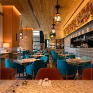 130席ある広い店内は、天井が高く開放感溢れる雰囲気。本店を思い起こさせるターコイズブルーの椅子がインテリアのアクセントに。オープンキッチンからの活気溢れる音も心地よい。DJブースがあるのもユニーク。