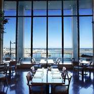 大きなガラス窓の向こうに青く輝く海を見渡せるシーサイドレストラン。高い吹き抜けの天井が開放感を演出。まるで異国のリゾート地にいるような雰囲気の中で、食事やスイーツをお楽しみいただけます。