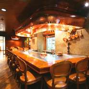 ライブ感に溢れ、豪快に焼く音を聴きながら料理を待つのも至福の時。頭上のフードは一枚の打ち出しの銅でつくられたこだわりの品。椅子やカウンターテーブルに至るまで、贅沢なひとときを演出してくれます。