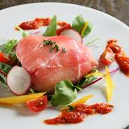 飛騨高山産モッツァレラチーズを贅沢に丸ごと１個生ハムで包みました。オリーブオイル・レモンで、さっぱりと味付けした野菜と一緒にお召し上がりください。