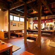 店内は木のテーブルや床をはじめ、吹き抜けの天井からは梁がのぞき、心地良い木のぬくもりに包まれている【ぶたや　黒将】。あちこちに置かれた豚の小物は自由に手に取ることもでき、遊び心も満点です。