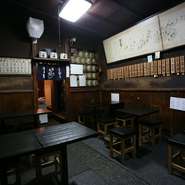 戦争により一時閉店。昭和25年に再営業してからでも60年を超える老舗。店内は改装した昭和39年当時のままで、叩きの床、ちょっとすすけた天井や壁、お酒の銘が書かれた木札などに歴史を感じます。