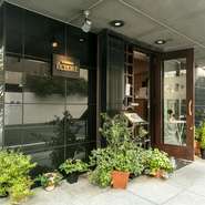 築地駅より徒歩2分と便利な場所にありますが、大通りより1本中に入った静かな通りに位置している【レストラン　エクロール】。シックな黒い壁に豊かに飾られた自然の緑が魅力的です。