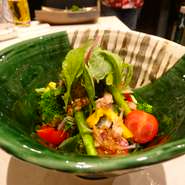 グリーンの葉物野菜やアスパラに、赤いトマトや黄色いパプリカを彩りよく盛り合わせ。オリーブオイルとアンチョビの風味が豊かな自家製ドレッシングをかけて。季節野菜がモリモリ食べられるヘルシーメニューです。