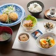 写真は春キャベツのメンチカツ、卵の袋煮、自家製胡麻豆腐など小鉢5品とお漬物、お味噌汁のメニュー。お料理はどれも季節の素材を生かしたやさしい味わい。奈良産ひのひかりのもっちりしたご飯の味を引き立てます。