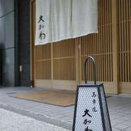 暖簾の字は、京都「妙心寺」の住職さんに筆をとっていただきました。また内装は、茶道石州流（せきしゅうりゅう）の茶室設計士によるもの。千家古流家元に生けていただく季節の花で、お客様をお迎えします。