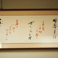 店内に飾られた額入りの書は、店主の師である片倉康雄氏が80歳の時に筆をとったもの。「何でもない　ありふれた　手打ちそば」と書かれた書は、今も店主が初心を思い返す言葉だと言います。