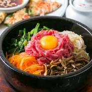 韓国の混ぜご飯のことで、石の器にご飯やナムル、キムチ、肉、たまごなどを入れて食べる料理です。おこげも美味しいので、具材とご飯をすべて混ぜ、石の熱で少し焦がしてから食べるのがおすすめです。