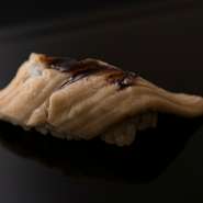 長崎県対馬海域の天然穴子で仕立てる自慢の握り。あらかじめ煮た穴子を笹の葉の上に乗せて、お客様の前で焼き上げてから握ります。とろける食感と焼いた香ばしさが極上の味わいです。※『おまかせコース』の一例です