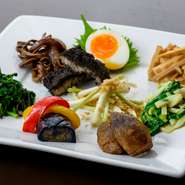 中央の『豚肉の黒ごま蒸し（ミヌダル）』は冷めても美味しい琉球王朝の伝統料理。『島らっきょう』『田芋（ターム）』など、季節ごとの沖縄の旬の味も盛りだくさんにお届けします。