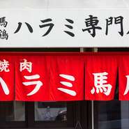 白い屋根に赤い暖簾が目を引く【焼肉 ハラミ馬鹿】の店頭。昔ながらのレトロな雰囲気が印象的です。店内に入ったところにキッチンがあるため、料理人が一番最初に元気よく出迎えてくれます。