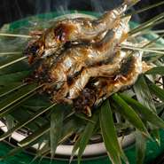 琵琶湖の鮎を頭を下にして油を垂らしながら頭はカリッと、身はふっくらと焼き上げます。中川一辺陶作のる炭鉢に、笹を敷き客前で笹の香りを鮎にまとわせて。初夏のご馳走です（写真は5月の献立の一例です）