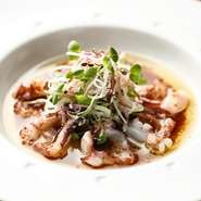 イタリア産の2種類のアンチョビと青森県産「福地ホワイト六片にんにく」をオリーブオイルで焦げる寸前まで熱し、生タコにかけて食べる一品。白ネギ、ミョウガ、桜かいわれなど、和の薬味でいただきます。