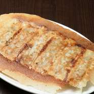 鉄板で焼き上げる、パリパリの羽根つき餃子です。とてもジューシーな食感も味わえます。新鮮な野菜と肉に特製のタレを加えて具を仕込み、手作業により一つずつ皮に包む手間暇をかけた一品です。