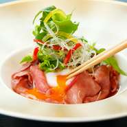リブロースを割下でさっと火入れをし、美しいロゼ色に仕上げています。通常煮る野菜は新鮮さを生かしサラダ仕立てにアレンジ。半熟卵を割りほぐせば、新たなすき焼きの誕生です。