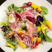 たっぷりの季節の野菜を盛り込んだ自慢のサラダ。野菜ベースでビネガーが効いた、さっぱり風味のドレッシングが野菜の味わいを引き立てます。生ハムはイタリア産で、滋味に満ちた塩気が野菜と絶妙にマッチ。