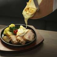 本場海外の味わいを楽しめるラクレットチーズは、自家製のウインナーとベーコンの2種類。チーズは塩分があるので、ベーコンは塩味控えめ。目の前で熱々のチーズをかけ流し、分厚いベーコンの食べごたえも最高！