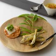 旬食材で彩るアミューズ。写真は一例で、北陸産小鰯に自家製ハーブの爽やかな衣をまとわせて揚げたベニエ、赤イカのチュイル、自家製白エビパウダーなどで隠し味をきかせた甘いトウモロコシの温製ポタージュ