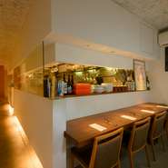 「大人の食堂」をイメージしたという空間は、白壁と木の風合いが調和したシンプルなデザイン。オープンキッチンで腕を振るうシェフの姿が垣間見え、美食への期待が高まります。