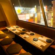 駅近ながらビルの最上階にある店内は、街の喧騒を忘れさせるシックで落ち着いた空間。温かな間接照明に包まれた掘りごたつ席からは、煌めく街の夜景が望め、訪れた人たちを非日常の世界へと誘います。