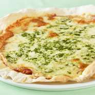 生地は国産小麦を使用したクリスピータイプで、シェフの手づくり。ガス窯で焼き上げたパリッとした食感と、自家製トマトソースの酸味やチーズのコク、バジルの香りが絶妙なバランスの逸品。フル／ハーフ