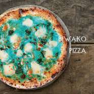 薪窯で職人が焼き上げたピッツァのなかでも、圧倒的人気のびわこピッツァは琵琶湖のスジ海老に桜えびや生しらすを加え、香ばしい仕上がりに。青色は天然素材のバタフライピーから。美味しい上に映えると評判です。