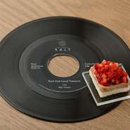 レコード針の先についたダイヤモンドチップに見立てたカナッペ。坂戸市の無添加生ハムの塩気を、煮詰めたバルサミコ酢とイチゴの酸味が引き立てるアミューズです。エシャロットやくるみなどがリズミカルに奏でます。