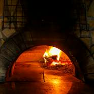 石窯で薪を焚くと内部は500度もの高温になります。ピザを窯に入れたら輻射熱で2～3分、目を離さずほどよい焼き目をつけ、最後に薪の煙を纏わせて。薪窯ならではのスモークが薫ります。
