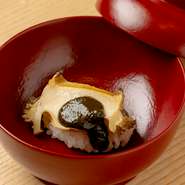 季節の食材があしらわれた、もち米の飯蒸し。使用される旬の食材は、会席コースの金額と季節に応じて変わります。写真はアワビとアワビの肝醤油をのせた『ディナーコース24200円』で供される一品です。