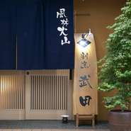 美しい格子の扉に下がる藍色の暖簾、屋号が書かれた一枚板など、随所に深いこだわりを感じられる割烹料理店。扉を開ければ10mもある檜のカウンターを設えたフロアがお目見えします。