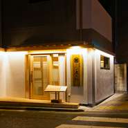 白木を使った漆喰壁の【三代目 庄之助】の新築のお店は角地。この時間、重厚な木の看板も魅惑的です。