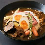 独自ブレンドのスパイスとルーをすべて燻し、こだわりの調合で仕上げた特製カレーは、名刺がわりのスペシャリテ。 4～5時間煮込んだ牛スジの旨みに薫香が心地よく絡みます。旬野菜や玉子の燻製を添えて。