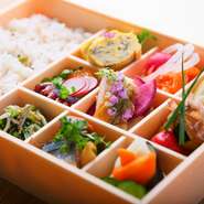 前日までの予約で楽しめるお弁当なら、日替わりおかず9種で旬の食材を存分に味わえる『一汁九彩膳』をご自宅やお勤め先でも楽しめます。ふたを開けた瞬間に笑みが溢れる彩り豊かなお弁当は、配達も可能です。