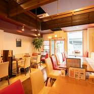 暖色の間接照明が、ゆったりとした時間を演出している店内。木目調のテーブルを中心としたナチュラルな雰囲気に、白と赤でカラーリングされた椅子がオシャレ感を引き立たせています。