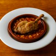 肉をオイルで煮込む『コンフィ』はビストロの定番メニュー。低温の油で5時間じっくり煮込んだ鴨モモ肉が主役の一皿です。フランスの伝統的な家庭料理『カスレ』（鴨だしで炊き出した豆の煮込み）の上にのせて提供。