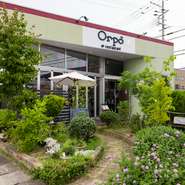 入口へと続く小路には樹木やハーブが植えられており、訪れる人たちを華やかに出迎えてくれます。この手入れの行き届いた緑の庭は、天井まで届くガラスの壁のおかげで、店内からも眺められます。