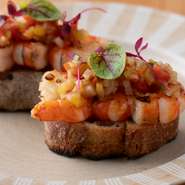 サルピコンは、魚介や野菜を細かく切ってドレッシングで和えたスペイン料理。【comodo】では、大きめの海老を使い、バケットにのせて提供しています。ビネガーの酸味とオリーブの旨みがたまらない一品です。