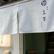 清潔感のある白暖簾が迎える【隠れ庵　玉響】。階段を上って扉を開ければ、心が落ち着くくつろぎの空間が広がります。「しばらくの間」などの意味がある店名どおり、ほんの少し日常を離れ、贅沢な時間を過ごせます。